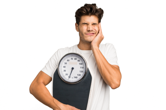 Young caucasian man holding a scale isolated covering ears with hands.