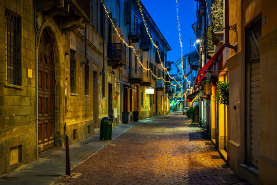 Old narrow cobblestone street illuminated with Christmas lights in Alba, Italy.