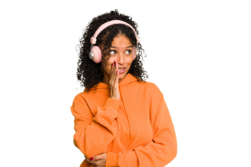 Young Brazilian woman listening to music with headphones isolated is saying a secret hot braking news and looking aside