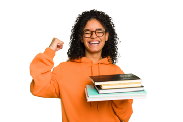 Young student woman holding a pile of books isolated raising fist after a victory, winner concept.
