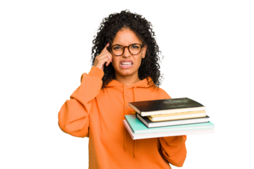 Young student woman holding a pile of books isolated showing a disappointment gesture with forefinger.