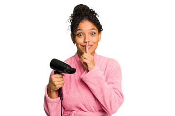 Young brazilian woman wearing a pink bathrobe holding an hairdryer isolated keeping a secret or asking for silence.