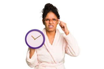Young brazilian woman wearing a pajama holding a clock isolated showing a disappointment gesture with forefinger.