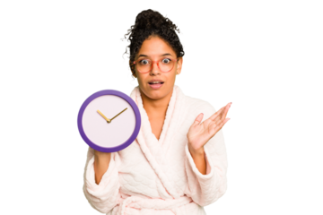 Young brazilian woman wearing a pajama holding a clock isolated surprised and shocked.