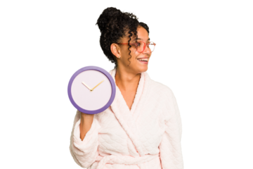 Young brazilian woman wearing a pajama holding a clock isolated looks aside smiling, cheerful and pleasant.