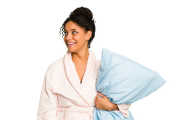 Young brazilian woman wearing a pajama holding a pillow isolated looks aside smiling, cheerful and pleasant.