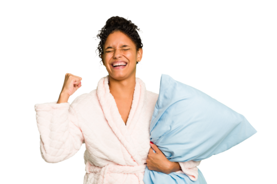 Young brazilian woman wearing a pajama holding a pillow isolated raising fist after a victory, winner concept.