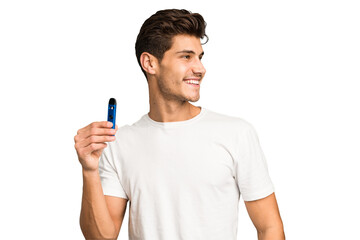 Young caucasian man holding an electronic cigarette isolated looks aside smiling, cheerful and...