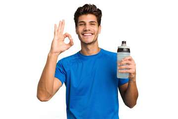 Young sport caucasian man holding a bottle of water isolated cheerful and confident showing ok...