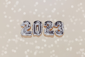 Christmas or New Year background. Beige color flat lay decorated with white paper glitter and silver shiny 2023 baloon numbers. Simple minimalistic greeting card.