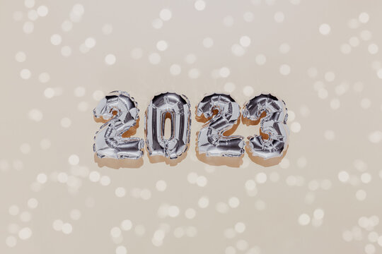 Christmas Or New Year Background. Beige Color Flat Lay Decorated With White Paper Glitter And Silver Shiny 2023 Baloon Numbers. Simple Minimalistic Greeting Card.