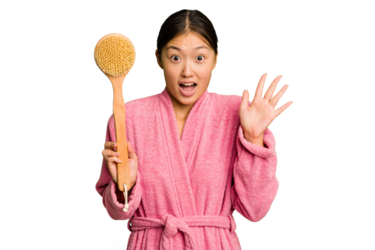 Young asian woman holding a shower brush isolated receiving a pleasant surprise, excited and raising hands.