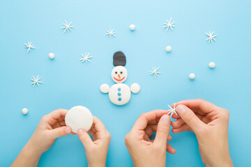Young adult mother and child hands modeling white snowman and snowflakes from clay on light blue table table background. Pastel color. Playing and spending time together. Top down view. Closeup.