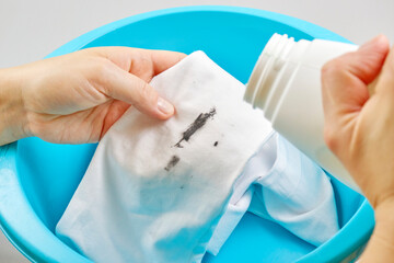a woman's hand holds a stain remover to remove a dirty stain from clothes. dirty spot for washing and cleaning concept