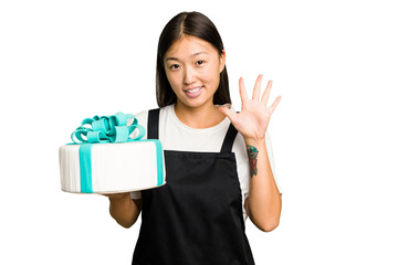 Young asian bakery holding a birthday cake isolated smiling cheerful showing number five with fingers.