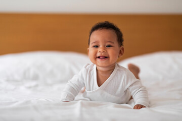 Baby Care Concept. Adorable Black Infant Child Relaxing On Bed At Home