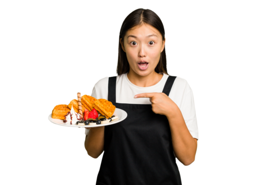 Young asian waitress woman holding waffles isolated pointing to the side