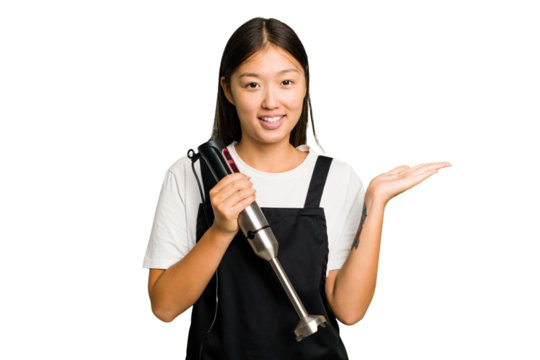 Young asian cook woman holding a blender isolated showing a copy space on a palm and holding another hand on waist.