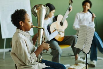 Side view of pre-teen schoolboy blowing wind instrument against two intercultural classmates...