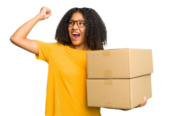 Young african american woman moving to other house while picking up a box full of things isolated raising fist after a victory, winner concept.