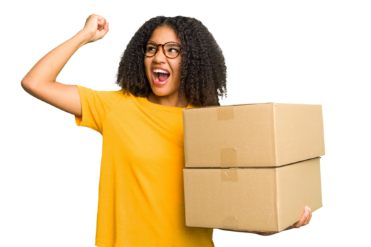 Young african american woman moving to other house while picking up a box full of things isolated raising fist after a victory, winner concept.