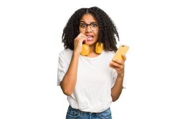 Young african american woman listening to music with yellow headphones isolated biting fingernails, nervous and very anxious.
