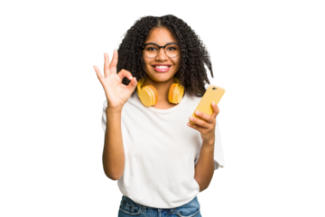 Young african american woman listening to music with yellow headphones isolated cheerful and confident showing ok gesture.
