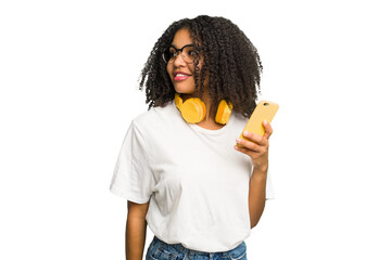 Young african american woman listening to music with yellow headphones isolated looks aside smiling, cheerful and pleasant.