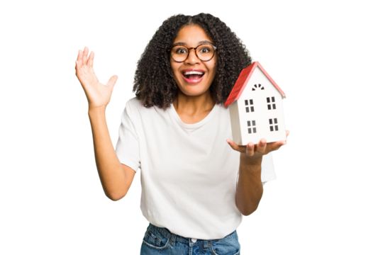 Young african american woman moving to a new home while picking up a box full of things isolated receiving a pleasant surprise, excited and raising hands.