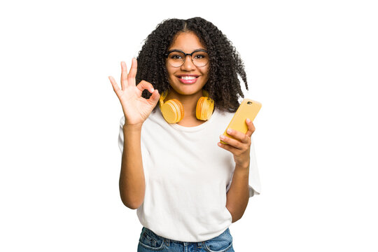 Young african american woman listening to music with yellow headphones isolated cheerful and confident showing ok gesture.