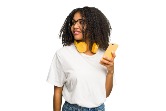Young african american woman listening to music with yellow headphones isolated looks aside smiling, cheerful and pleasant.