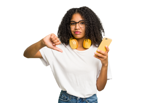 Young african american woman listening to music with yellow headphones isolated showing a dislike gesture, thumbs down. Disagreement concept.