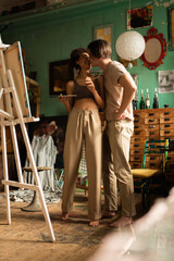 full length of barefoot interracial couple kissing near easel in art workshop with vintage decor.