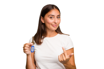 Young caucasian woman holding a home keys isolated pointing with finger at you as if inviting come closer.