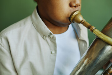 Close-up of pre-teen African American schoolboy in casualwear blowing trumpet during individual...
