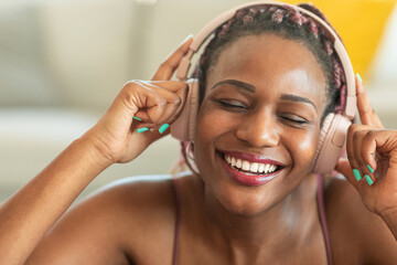 Happy african american woman enjoying music with closed eyes, touching headphones while resting...