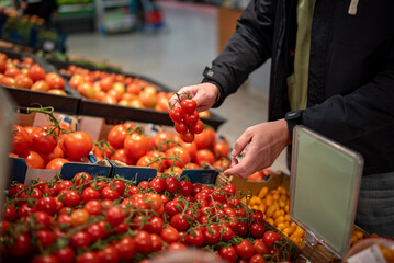 man hand holding cherry tomato in grocery store in supermarket