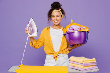Young fun housekeeper woman wear yellow shirt white t-shirt tidy up ironing clean clothes on board...