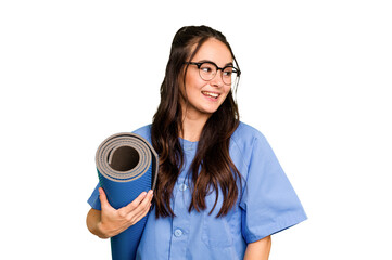 Young caucasian physiotherapist woman holding a mat isolated isolated on green chroma background looks aside smiling, cheerful and pleasant.