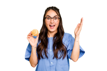Young caucasian physiotherapist woman holding a tennis ball isolated isolated on green chroma background receiving a pleasant surprise, excited and raising hands.