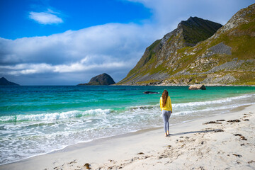 a beautiful long-haired girl enjoys the sunny weather on the famous paradise beach of haukland on the lofoten islands in northern norway; a beach walk in the norwegian fjords - obrazy, fototapety, plakaty