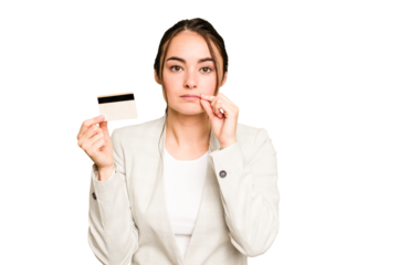 Young caucasian woman holding a credit card isolated on green chroma background with fingers on lips keeping a secret.
