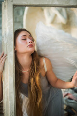 Fototapeta premium Time to go beyond. An angel girl with long hair holds a white frame and looks away. Portrait