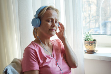 Naklejka premium Close up senior woman in blue headphones enjoying music with her eyes closed