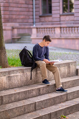 Focused adolescent boy reading a book outdoors
