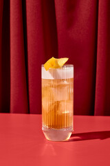 Classic cocktail whiskey sour with egg foam in highball glass on red background. Whiskey sour on coloured background in trendy style. Contemporary concept with alcohol beverage with shadow.