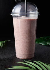 Strawberry shake in take out glass on dark background with leaves. Mock up drink in minimal concept...
