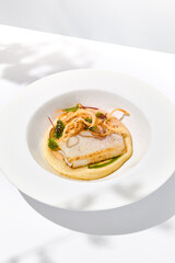 Roasted squid on mashed potatoes and crispy onion. Grilled squid with celery cream on white plate with shadows of leaves. Summer seafood menu. Roasted calamari in fine dining.