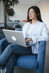 Naklejka premium Young charming female freelancer using laptop computer for distance job while sitting in modern coffee shop interior, beautiful Caucasian woman working on net-book during morning breakfast in cafe bar