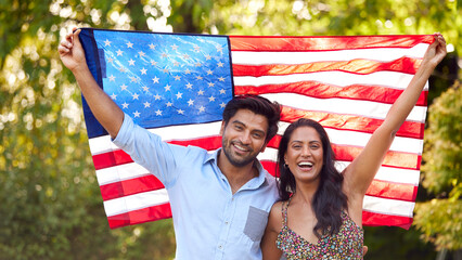Portrait Of Patriotic American Couple Holding USA Stars And Stripes Flag Outdoors In Garden